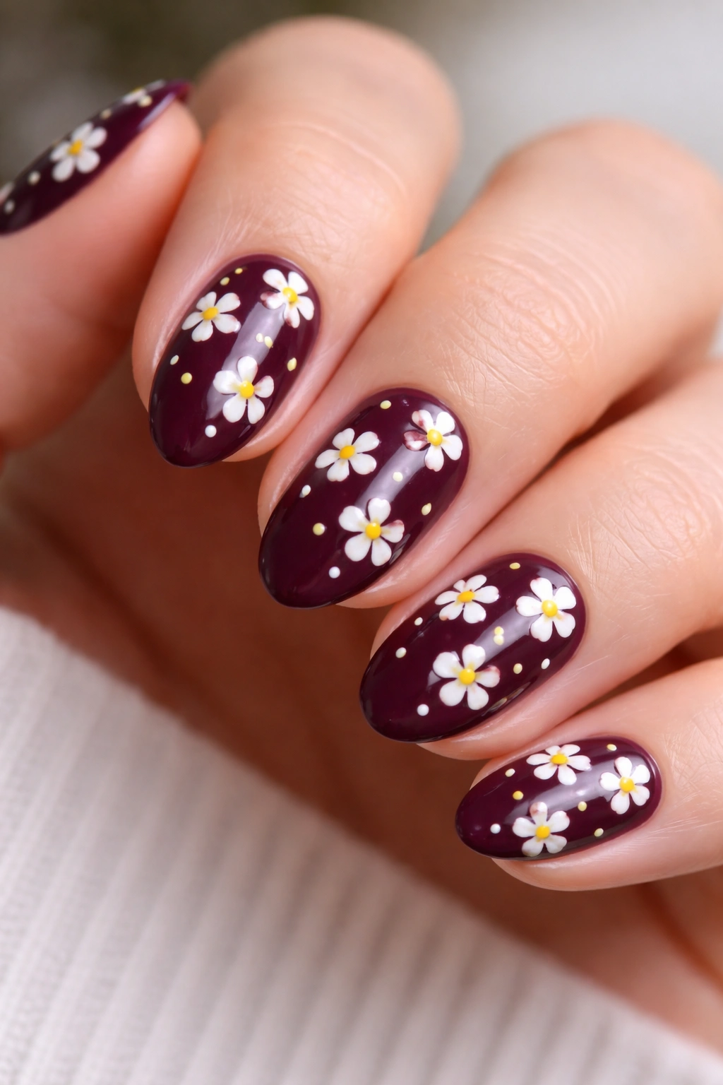 Close-up of short almond nails featuring tiny white and yellow blooms on a deep plum base.