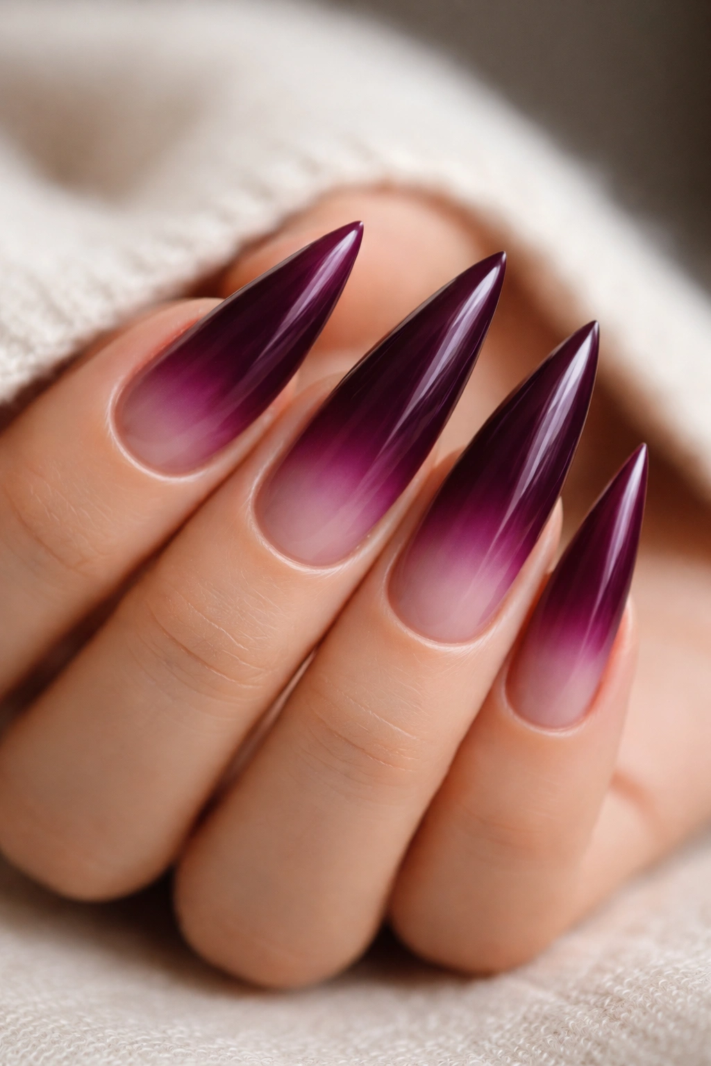 Close-up of deep plum ombré stiletto nails fading to nude tips under studio lighting