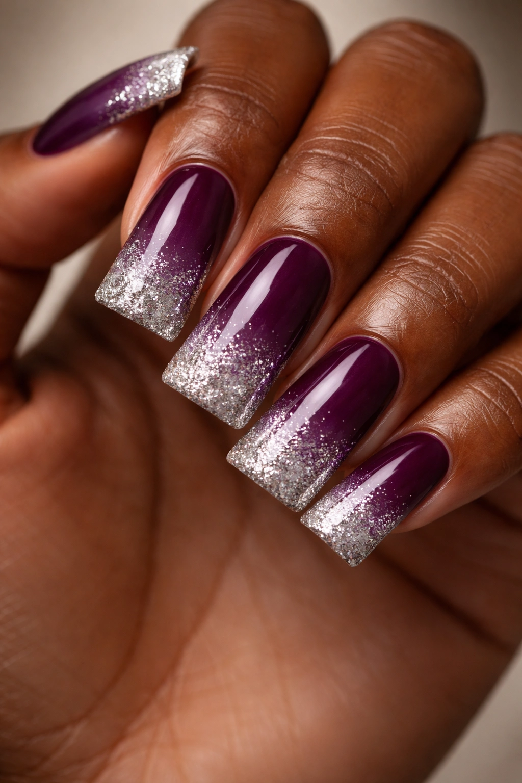 Close-up of plum duck nails with silver glitter ombre on dark skin