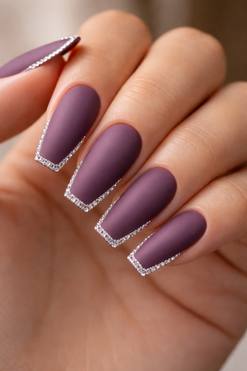 Close-up of matte plum coffin nails with rhinestone border
