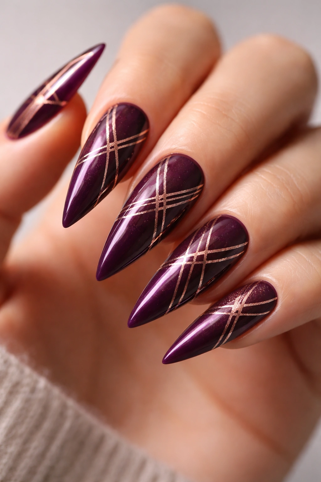 Close-up of deep plum nails with rose gold geometric lines