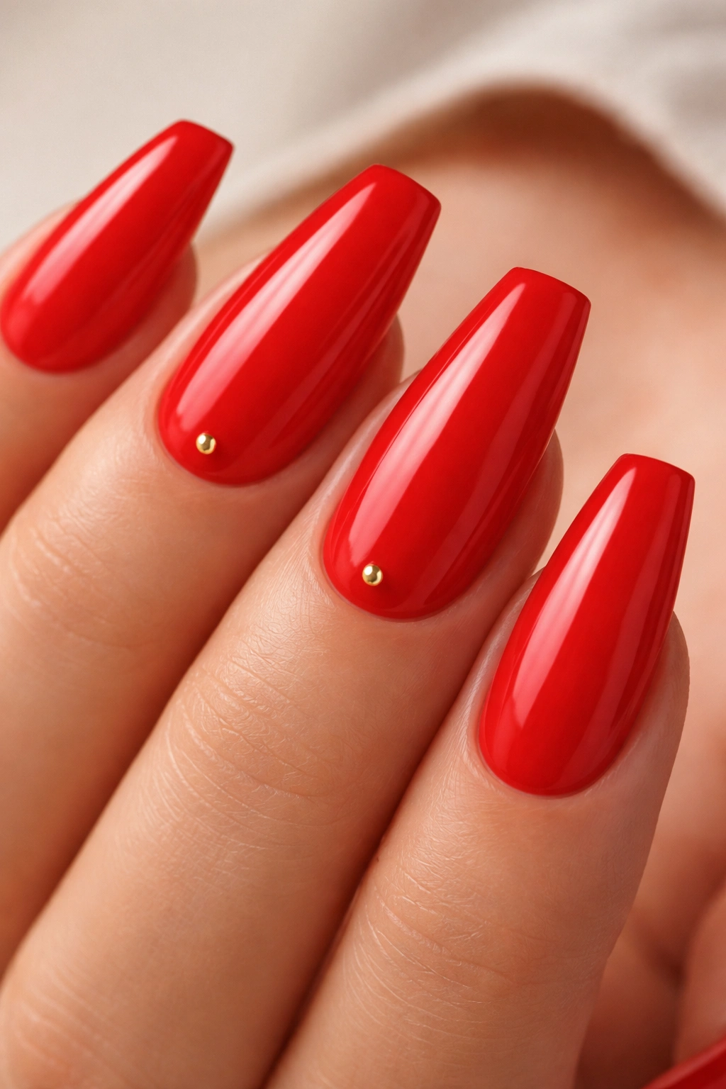 Close-up of poppy red nails with a tiny gold stud accent on accent nails near the cuticle.