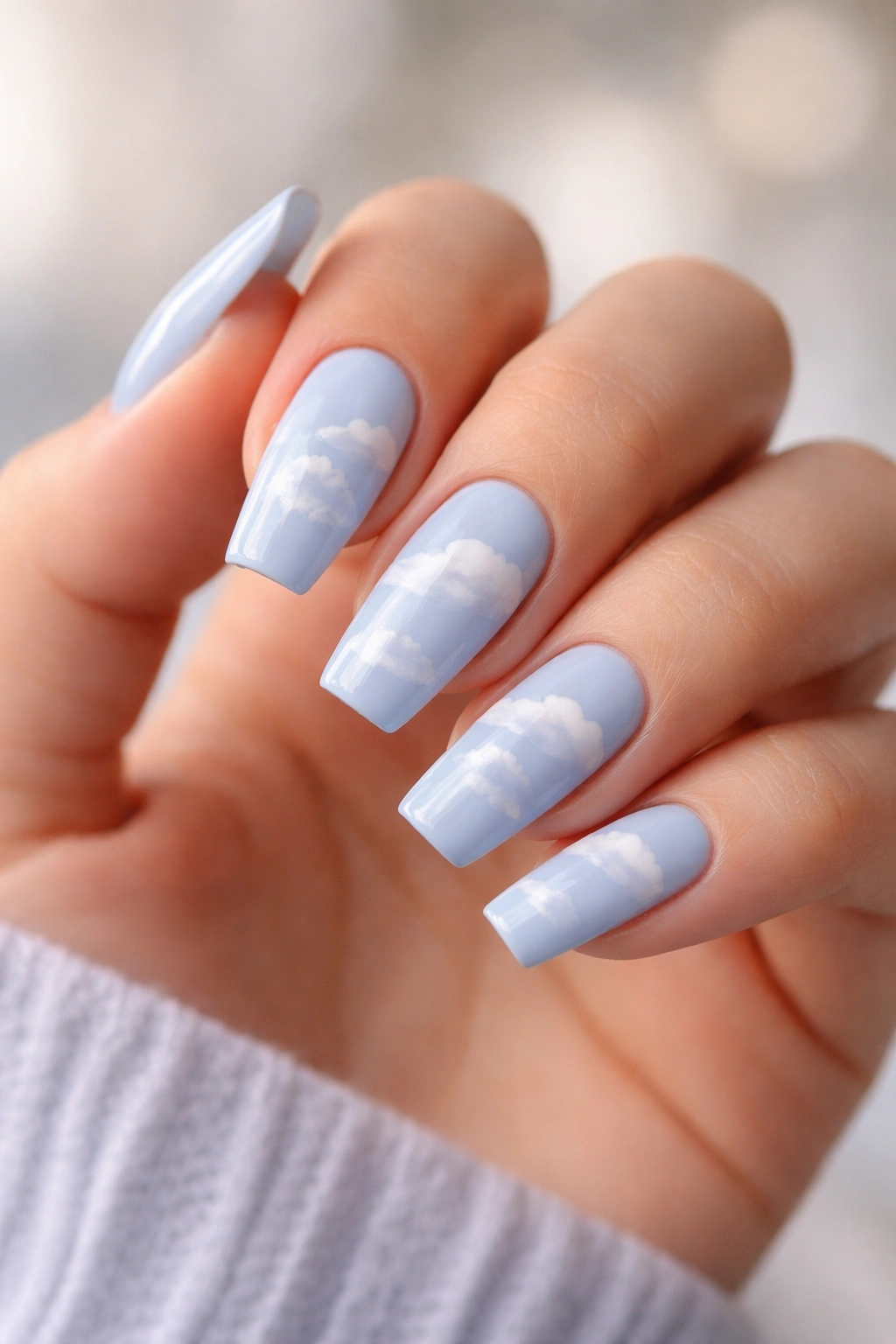 Powder blue coffin nails with white clouds on a bare hand