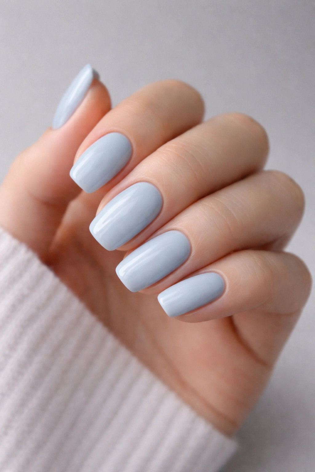 Close-up of short almond nails painted powder blue with a gray undertone and a clean square curve