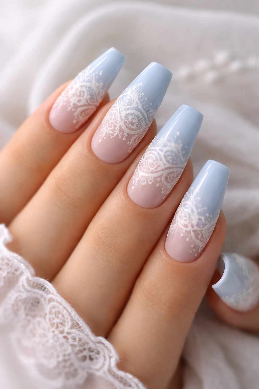 Close-up of powder blue coffin nails with white lace decals in a soft studio setting