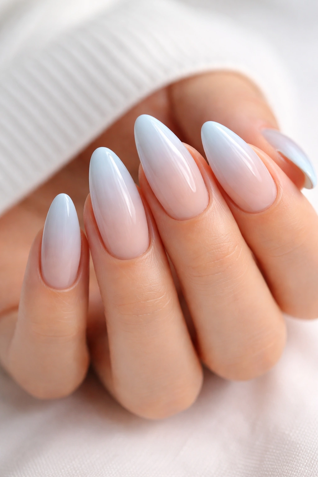 Close-up of powder blue ombre almond nails with nude base and pale blue tip.
