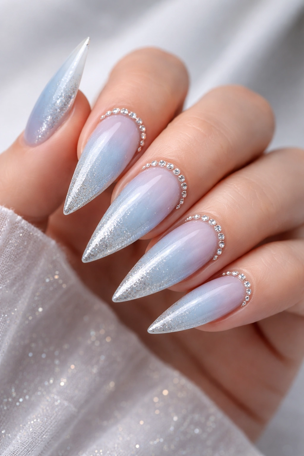 Close-up of powder blue to silver ombre stiletto nails with rhinestone border