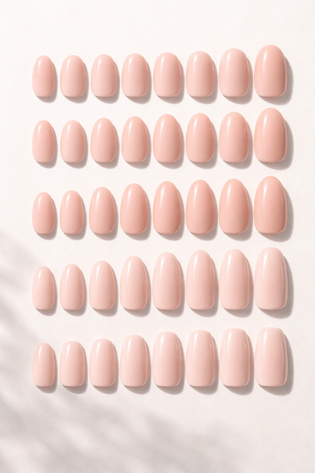 Row of press-on nails in round, oval, almond, squoval shapes arranged on a pale surface