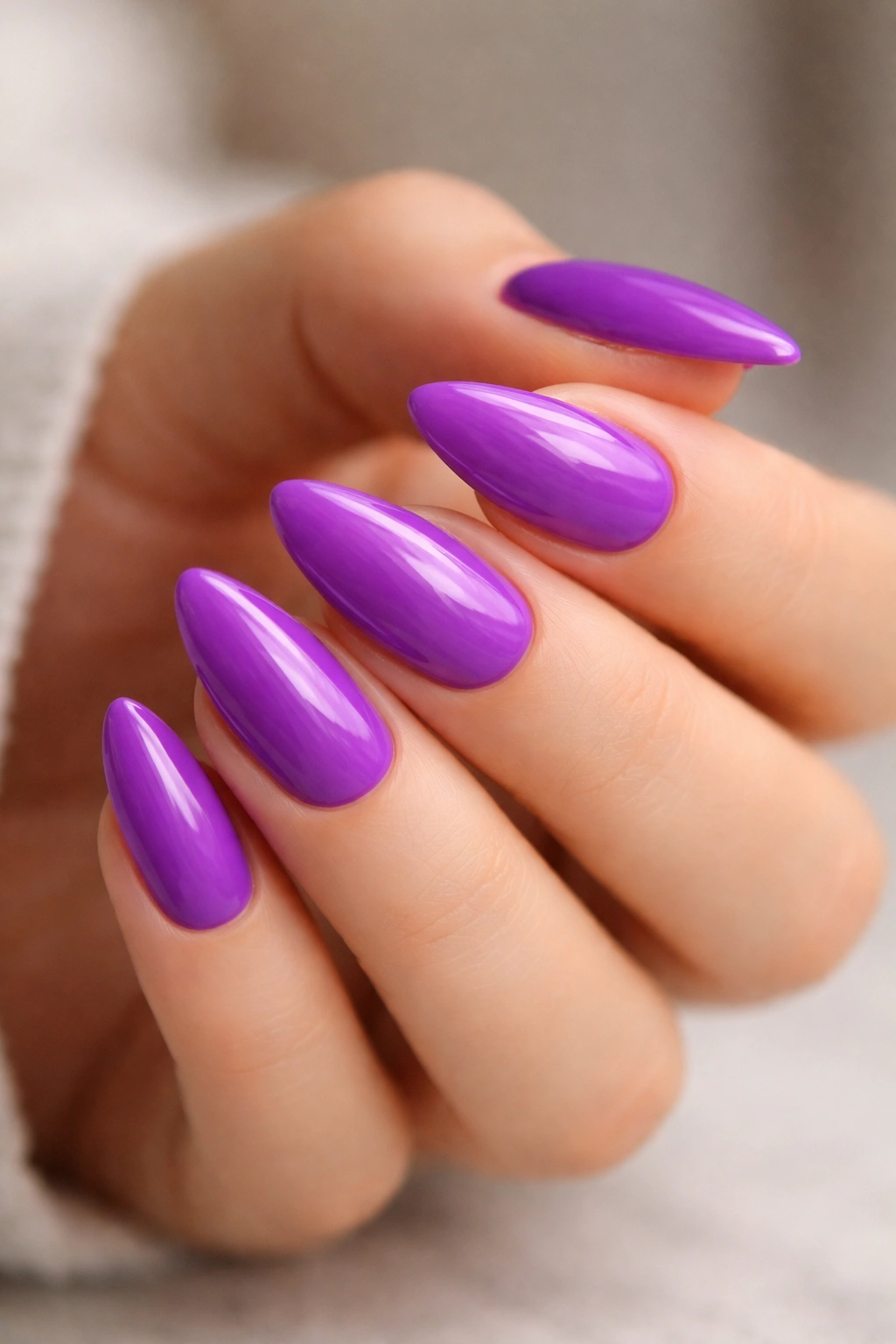 Close-up of bright purple almond nails with glossy finish on a neutral background