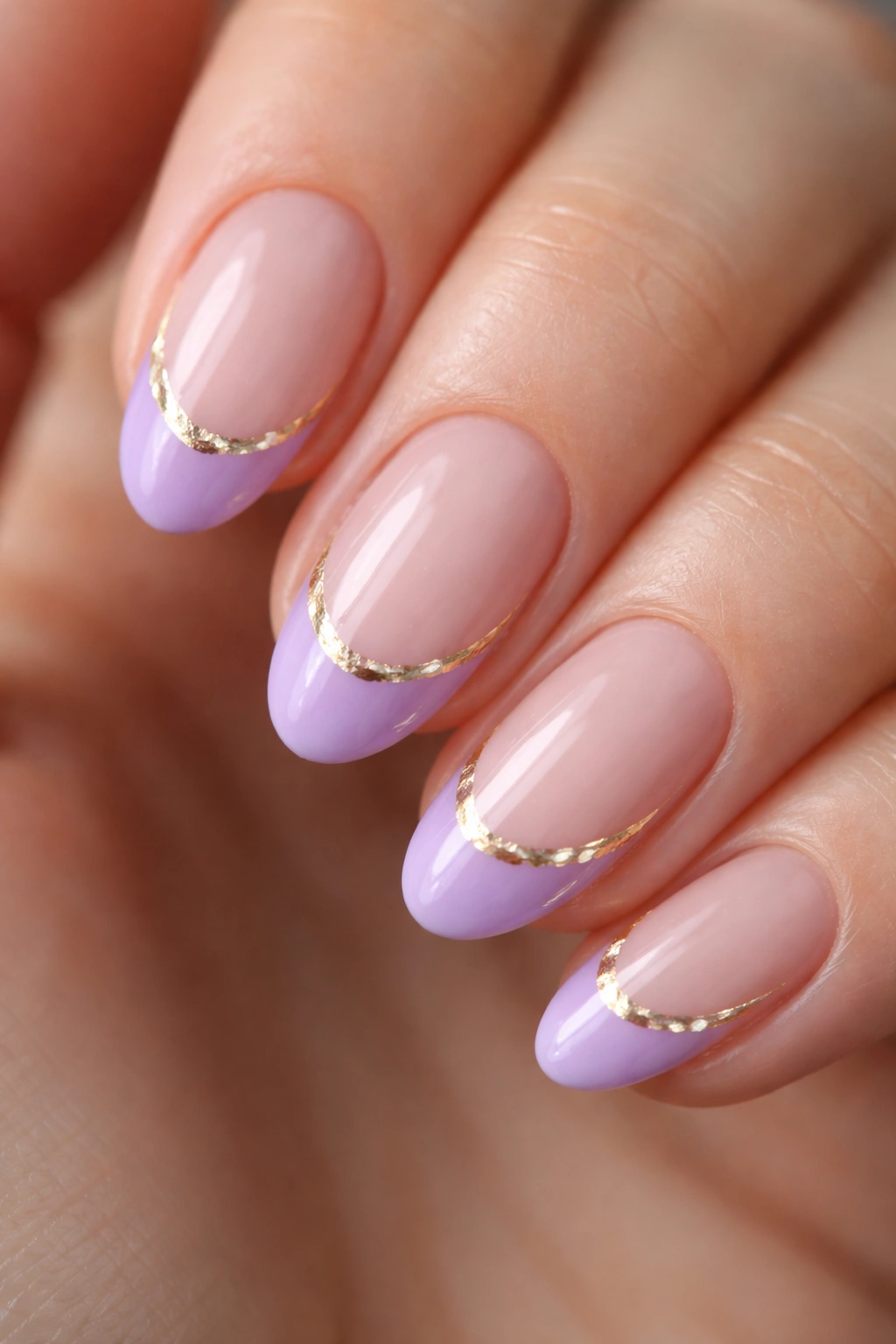 Close-up of a purple french tip with gold foil accents on a short almond nail