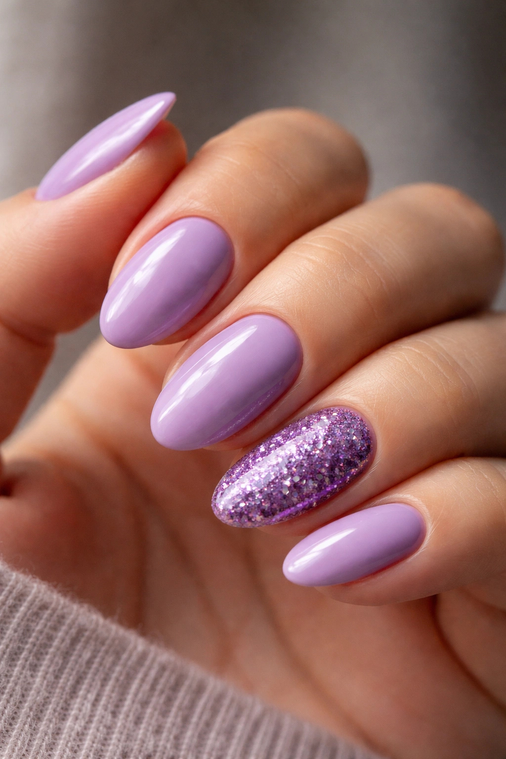 Close-up of short almond nails with purple glitter accent on one nail