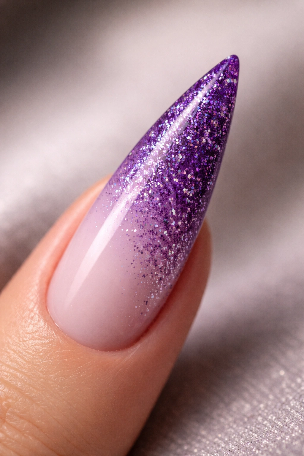 Close-up of a purple gradient stiletto nail with glitter fade