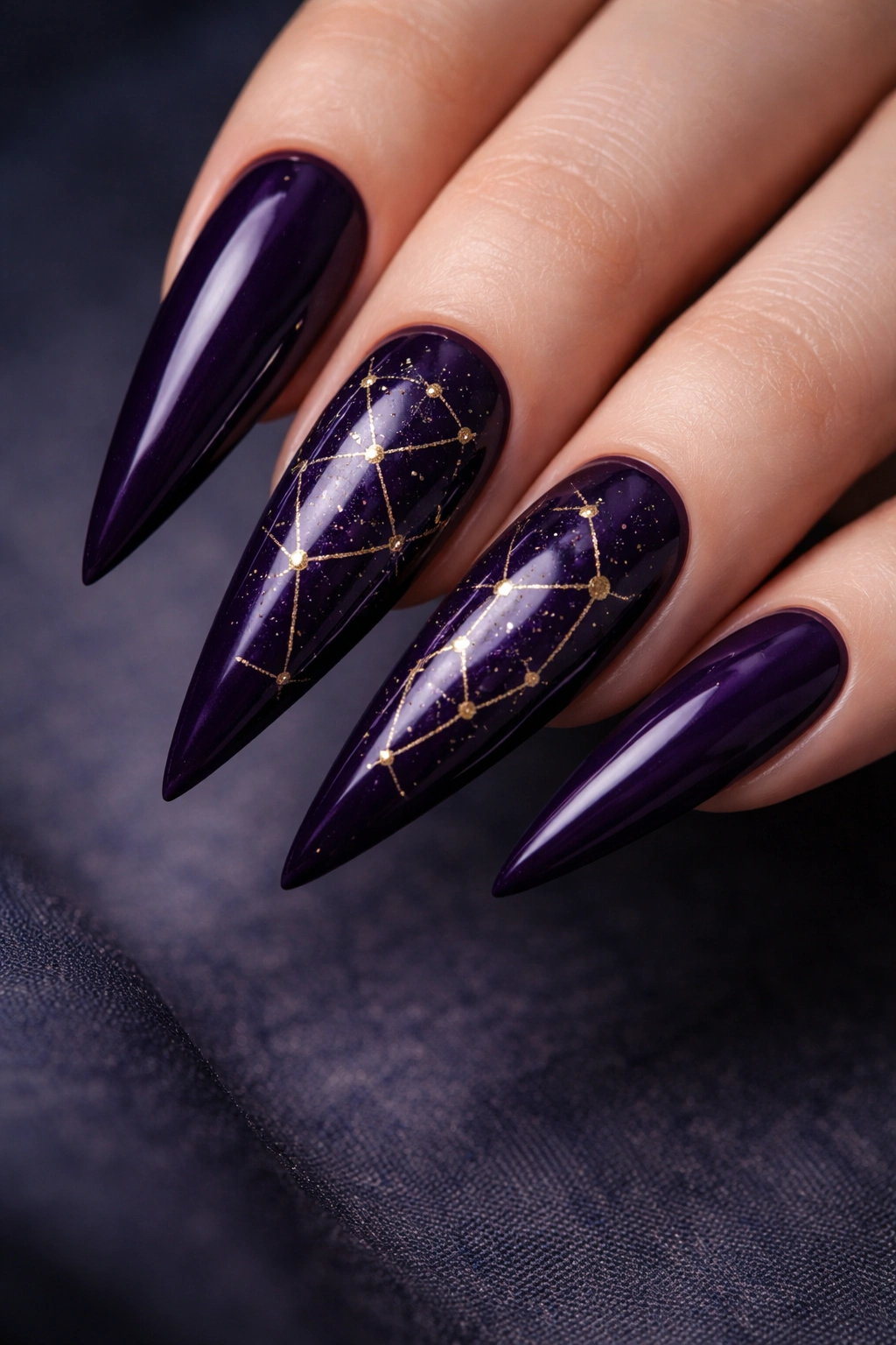 Close-up of dark purple stiletto nails with gold constellation dots and lines.