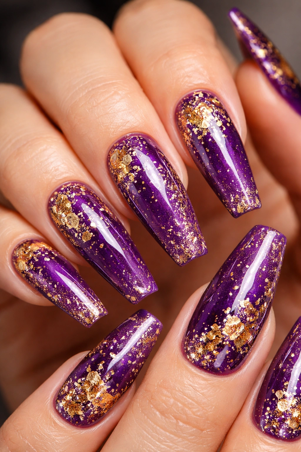 Coffin nails with purple base and gold glitter and foil accents in a close-up