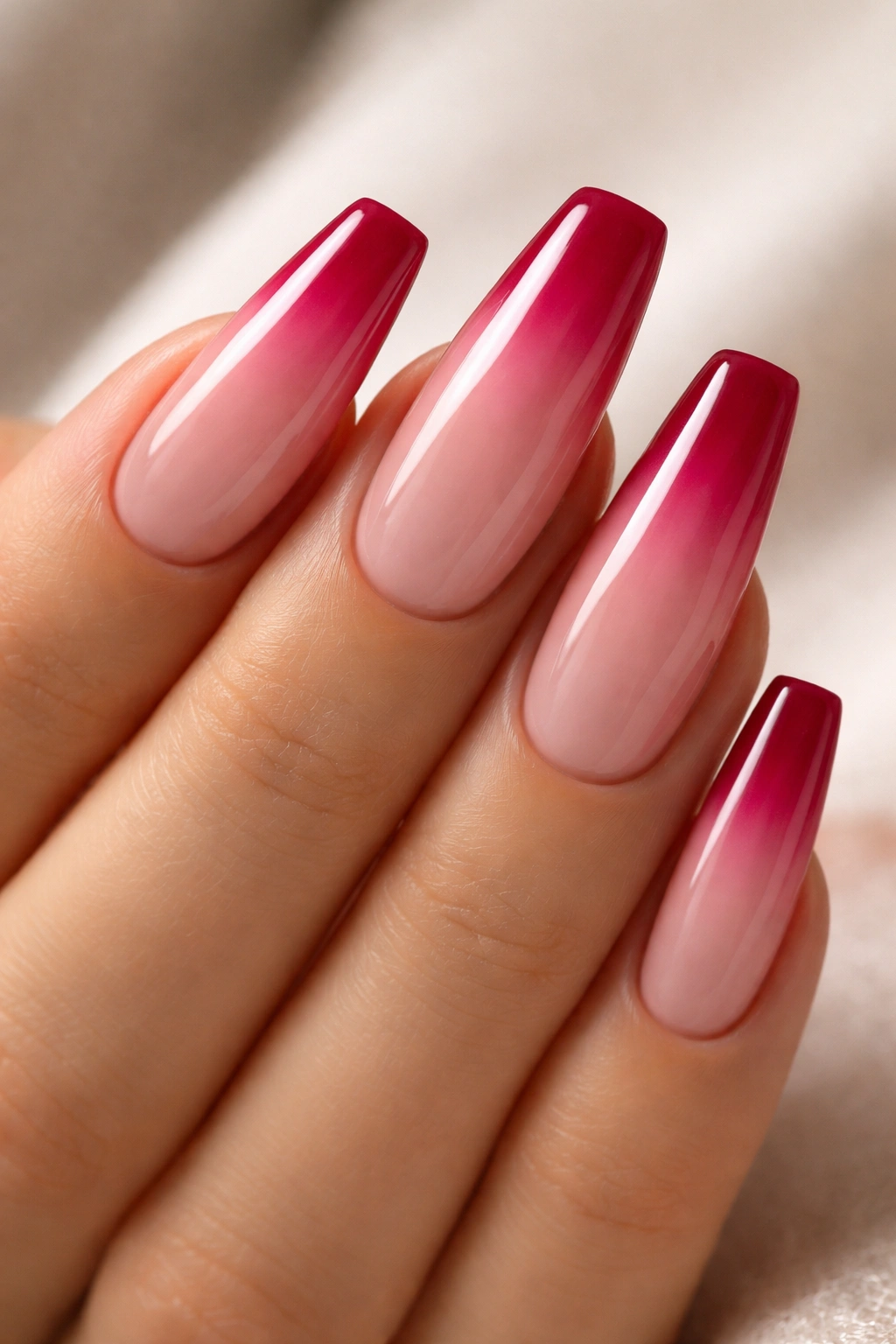 Close-up of raspberry ombré nails on a nude base with a sharp tip color and high gloss finish.