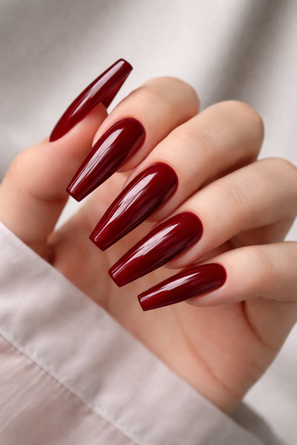 Close-up of glossy red coffin nails on pale hand.
