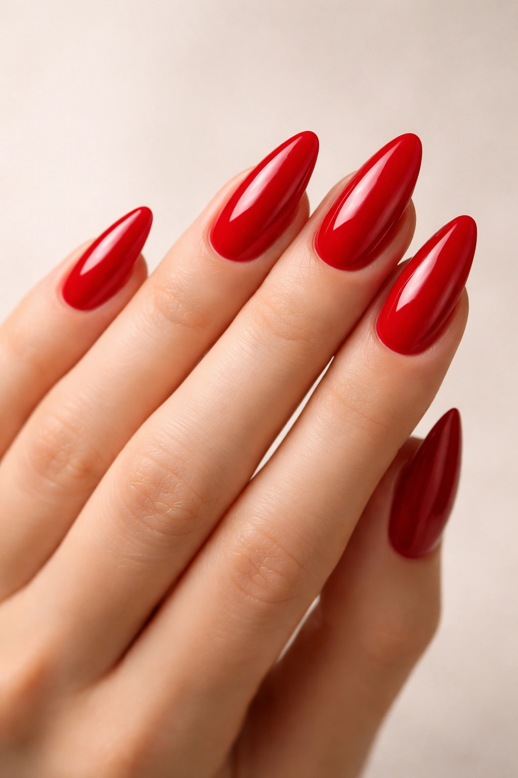 Close-up of red almond nails with glossy finish on a neutral background