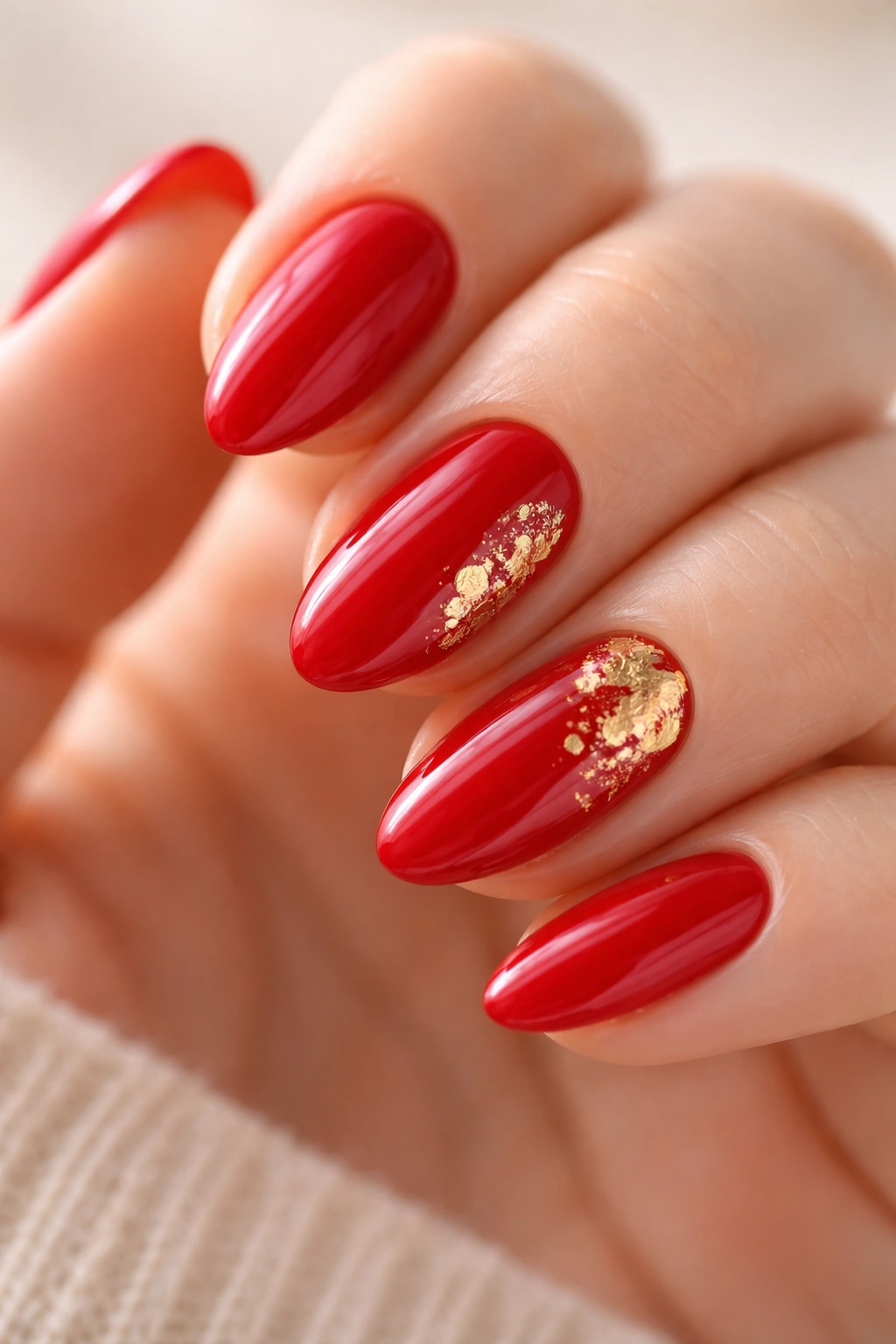 Short almond nails with red polish and gold foil accents