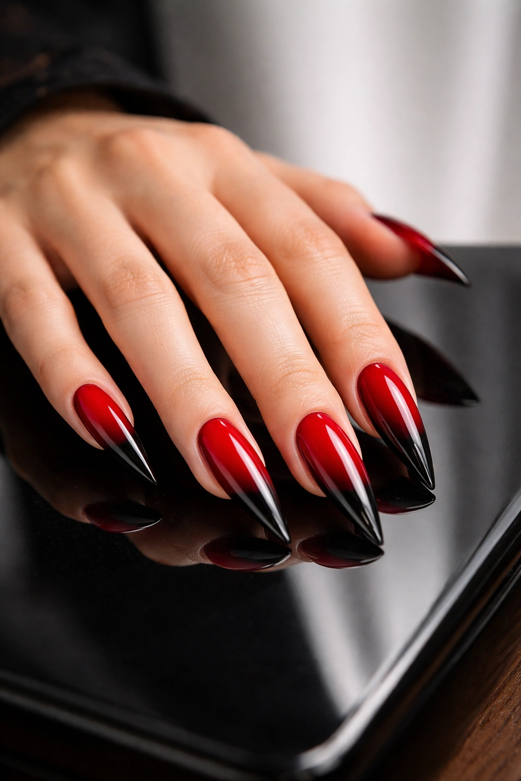 Hand with red and black stiletto nails on a reflective surface