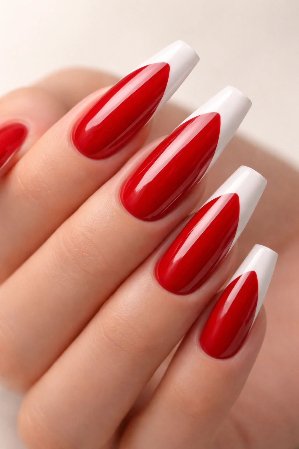 Close-up of red coffin nails with white tip negative-space design on a neutral surface