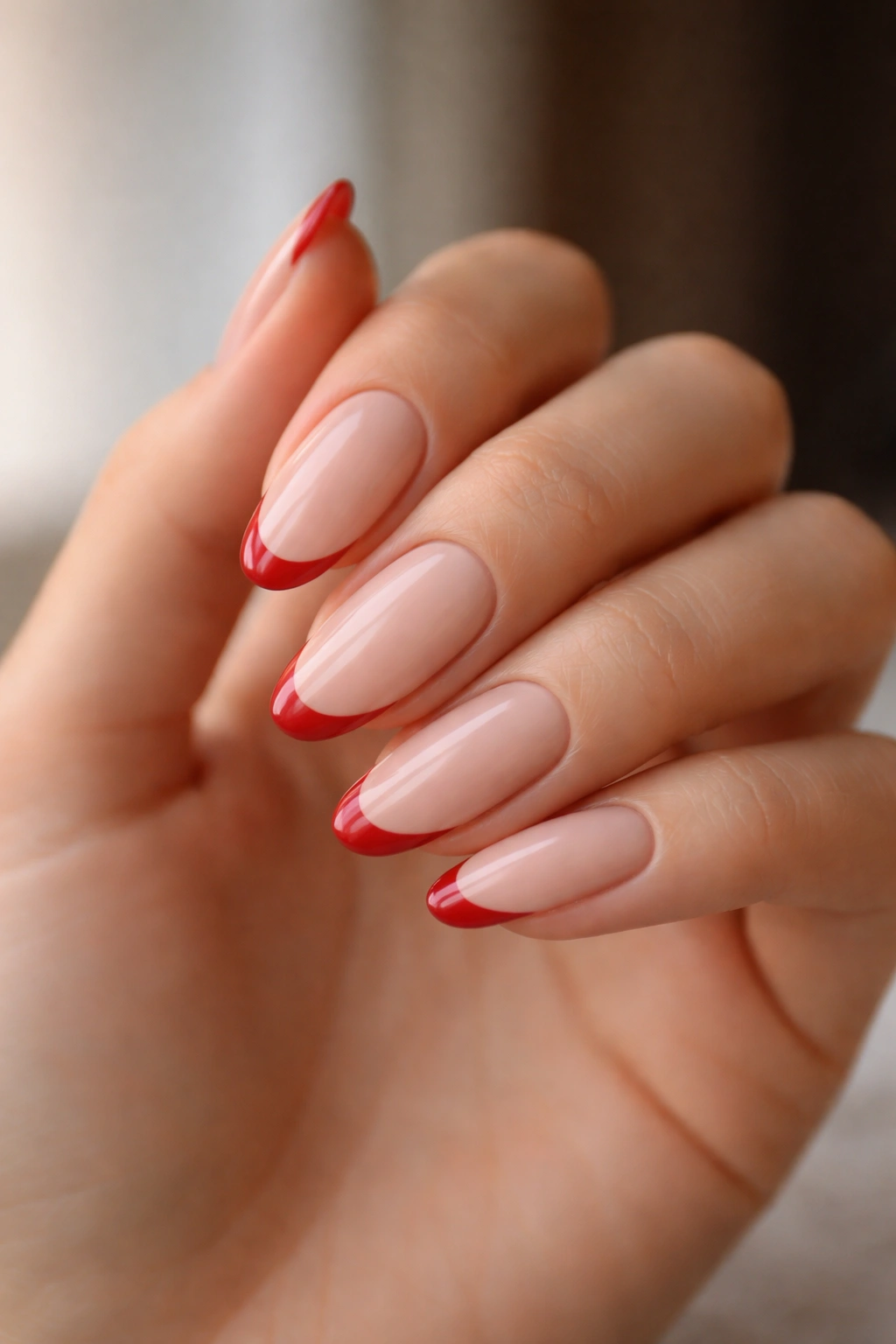 Close-up of nude oval nails with slim red French tips.