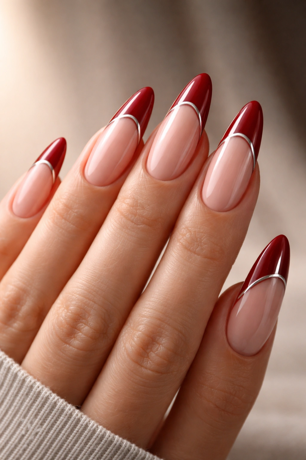 Close-up of long almond nails with deep red tips and a slender silver line along the edge