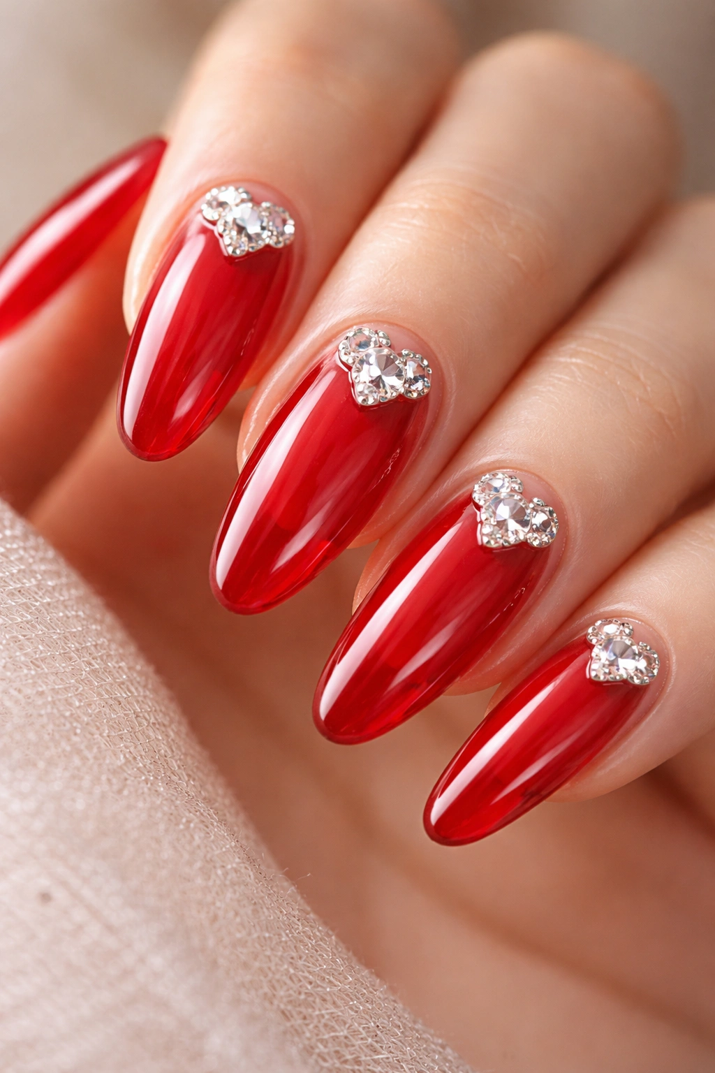 Close-up of red glass long oval nails with a tiny heart-shaped rhinestone cluster near the cuticle