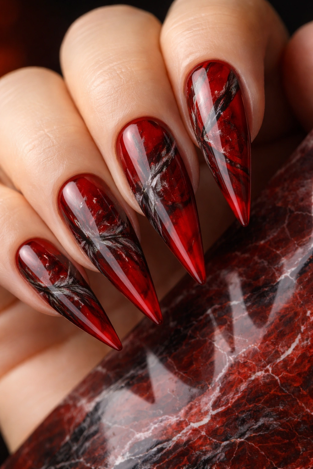 Close-up of red stiletto nails with black and gray marble veining
