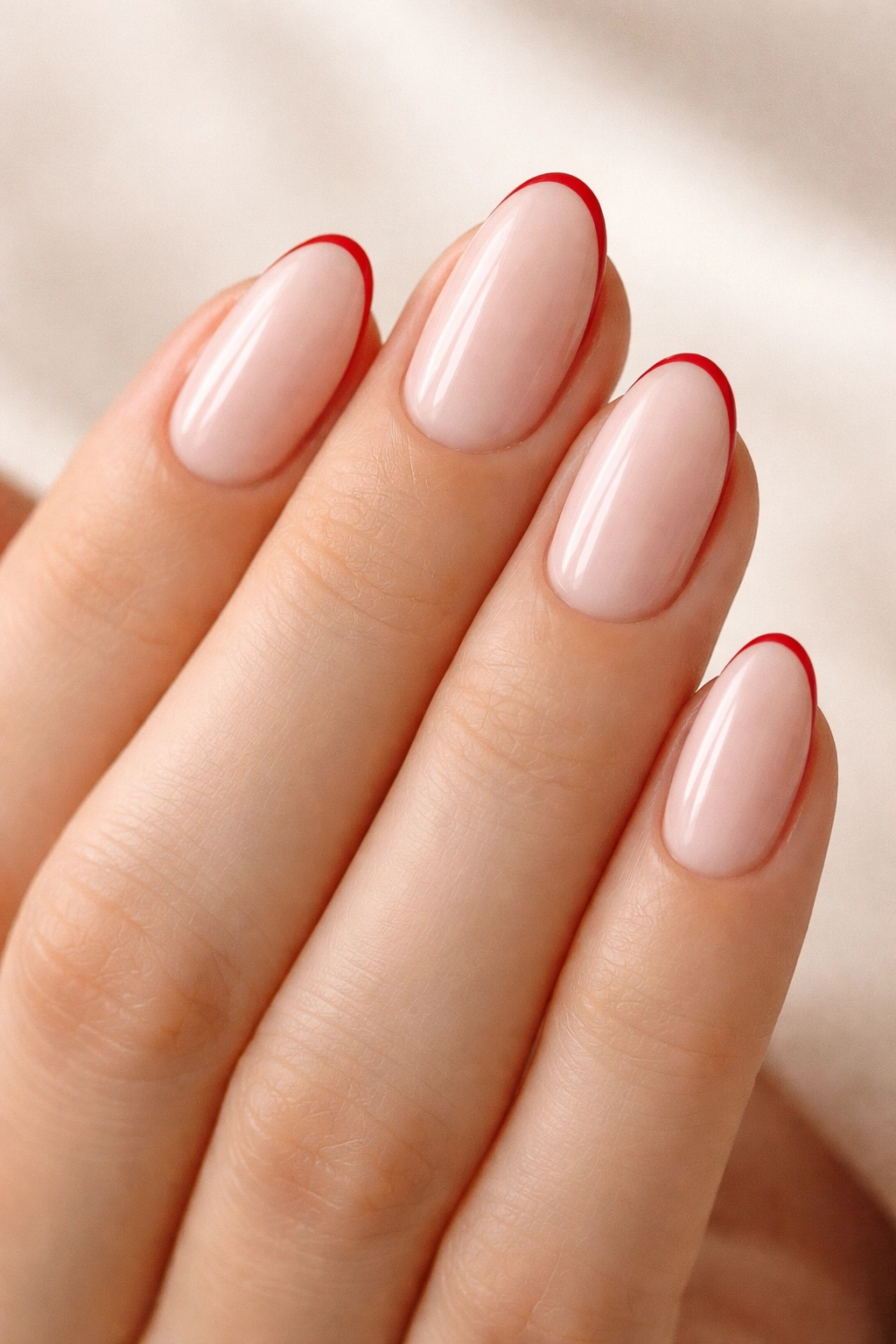 Close-up of red micro-French short almond nails with thin red tip.