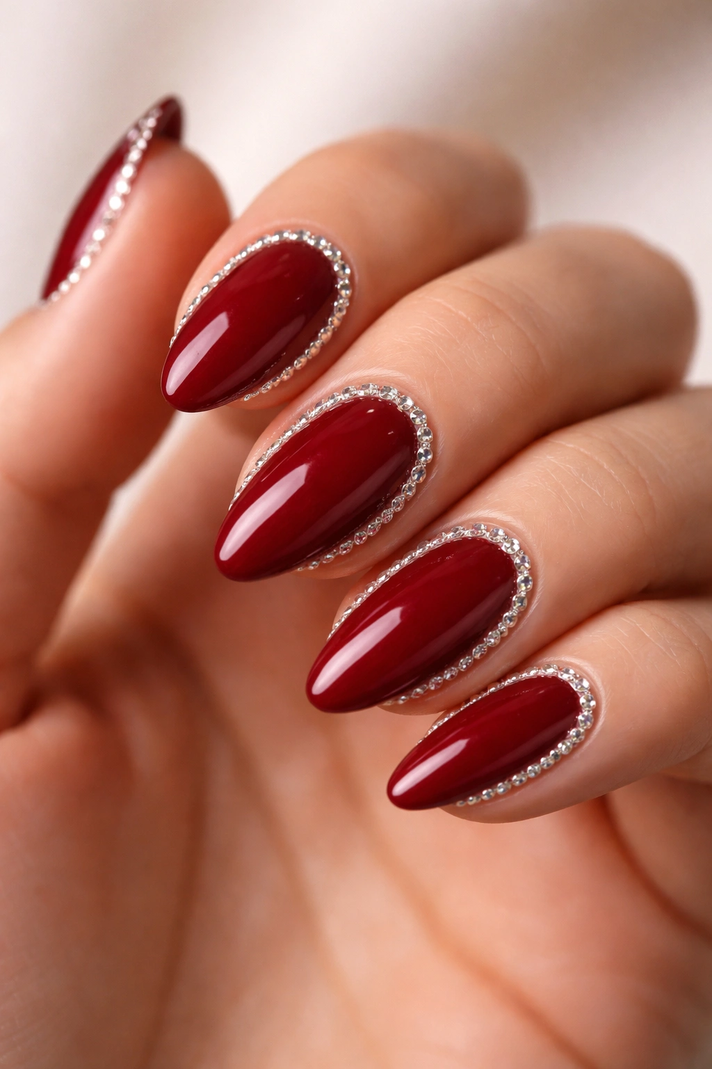 Deep red almond nails with crystal border along base and sides