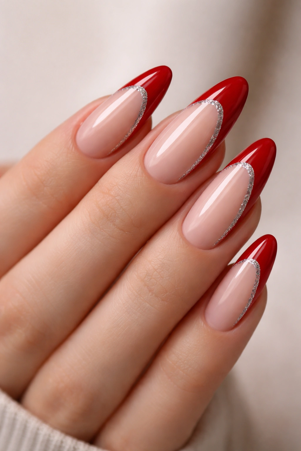 Close-up of almond nails with red side-swept glitter tips on a neutral background