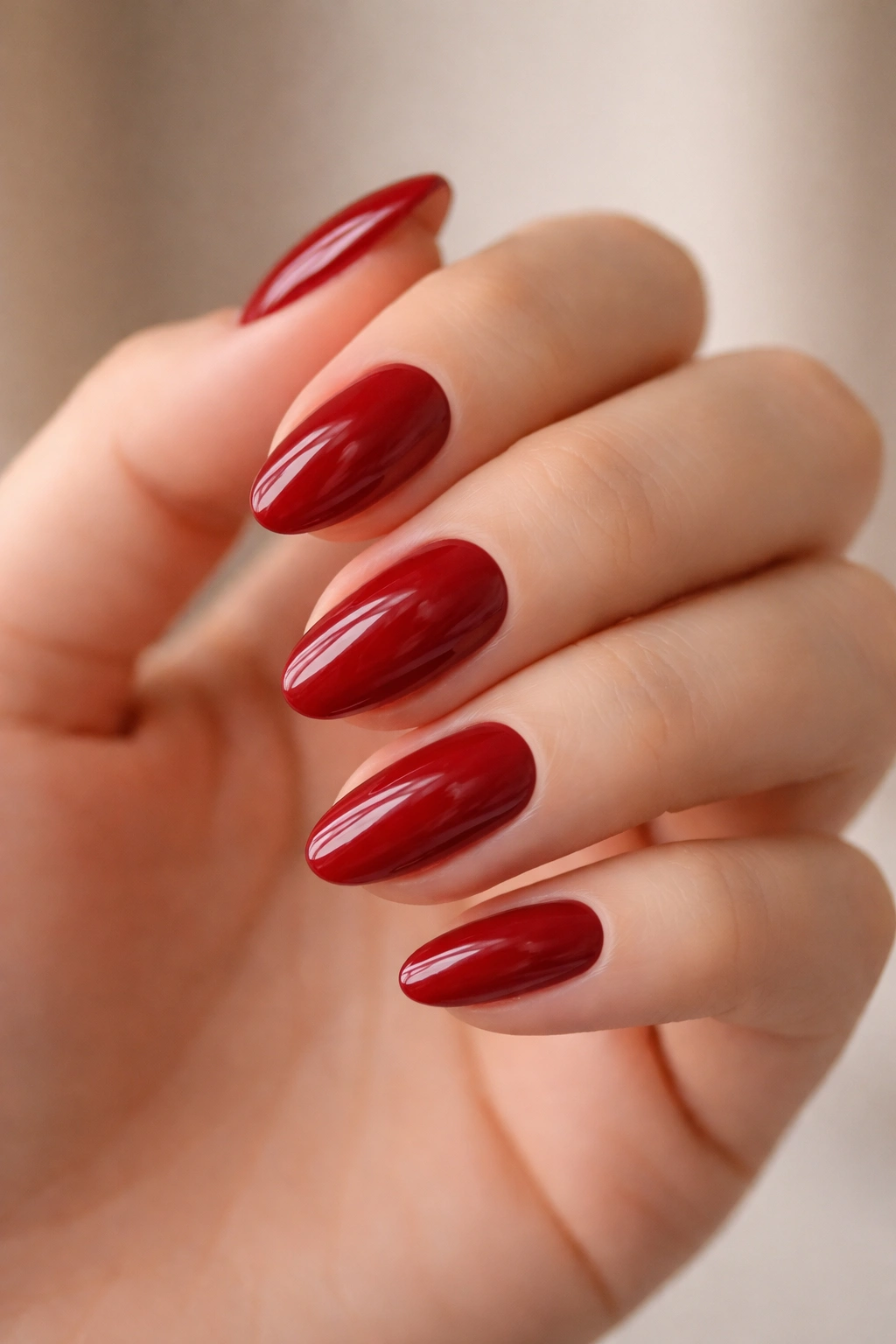 Close-up of short almond nails painted deep red with glossy finish