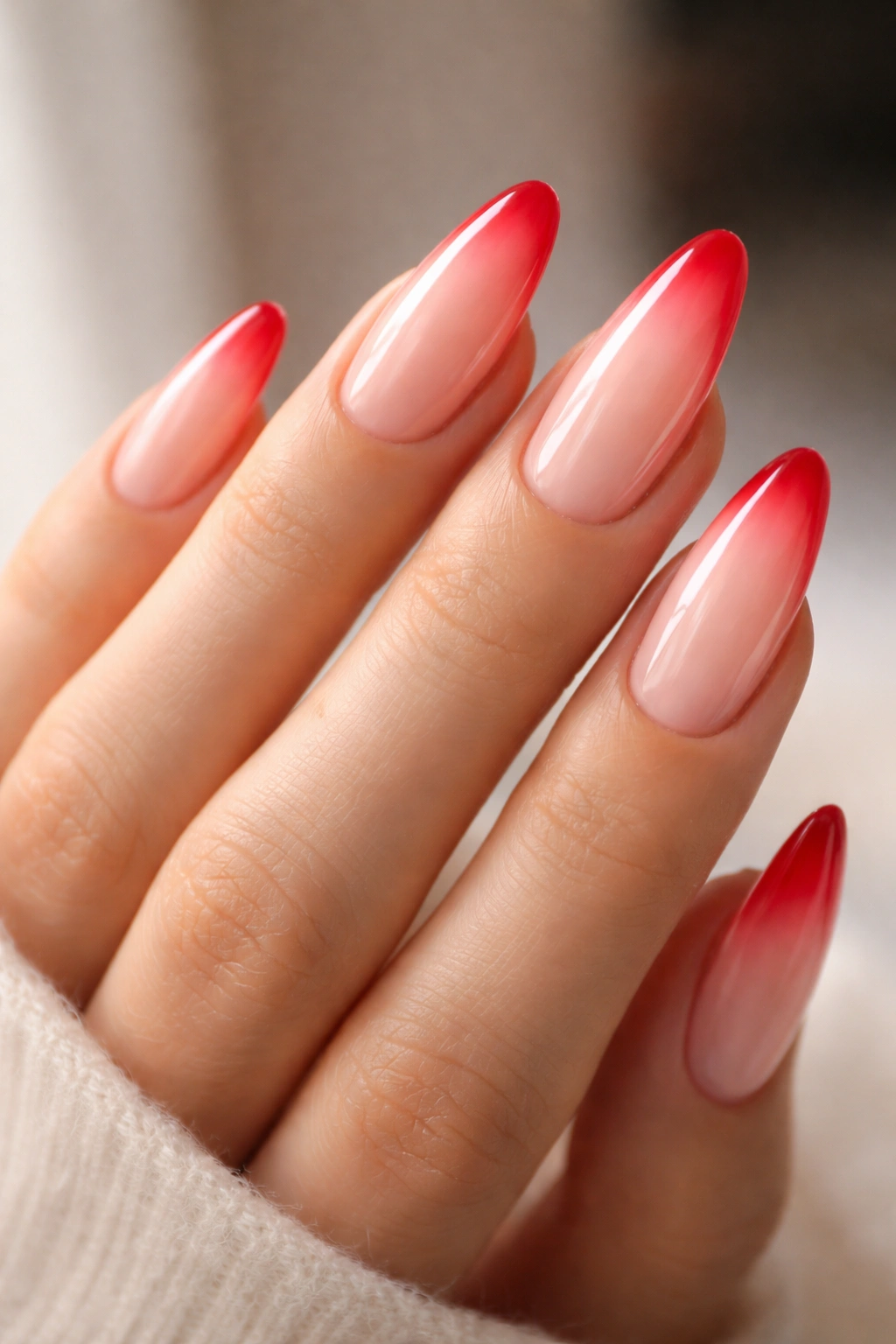 Close-up of long almond nails with a soft red aura around the tips on a neutral base