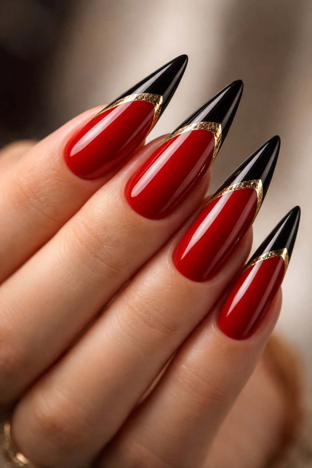Close-up of red stiletto nails with black tips and gold foil detail