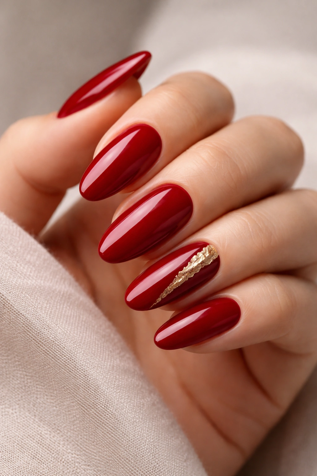 Close-up of long oval nails in deep red with gold foil accent on one nail