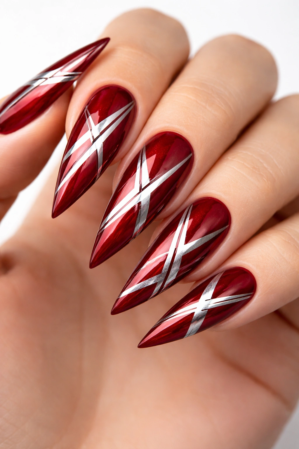 Close-up of deep red stiletto nails with silver geometric lines on a clean backdrop