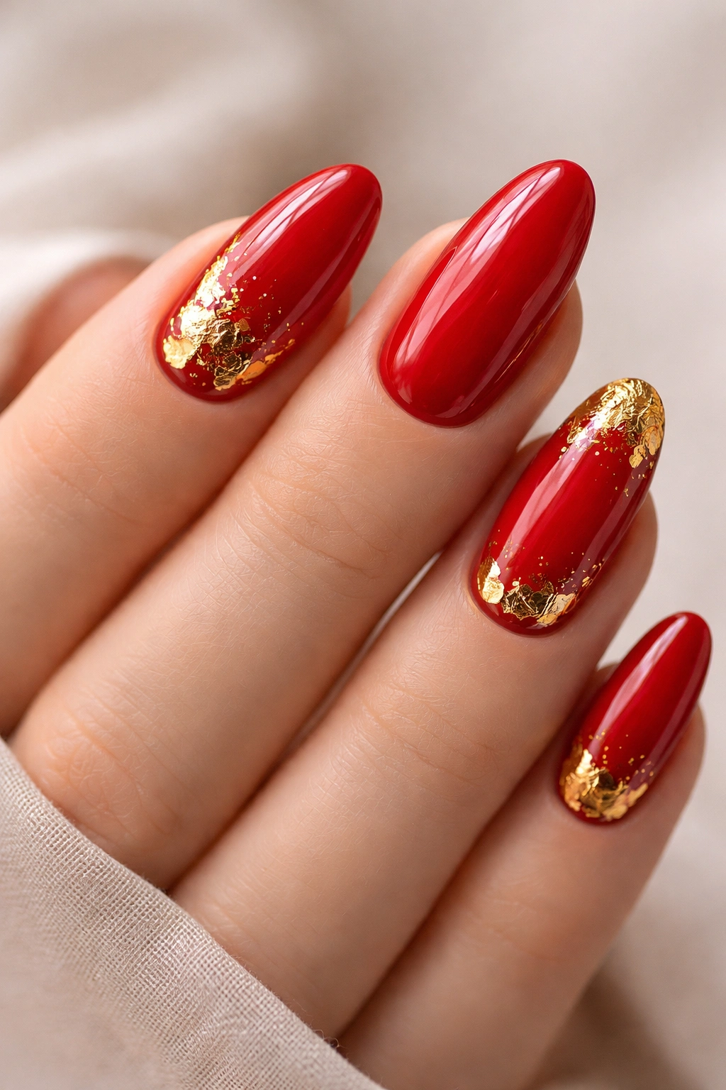 Close-up of red nails with irregular gold foil accents near tips
