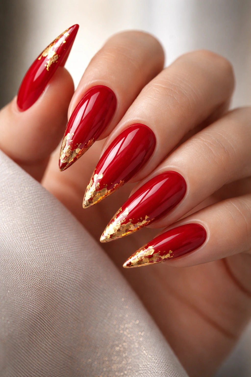 Close-up of red stiletto nails with gold foil accents on a hand