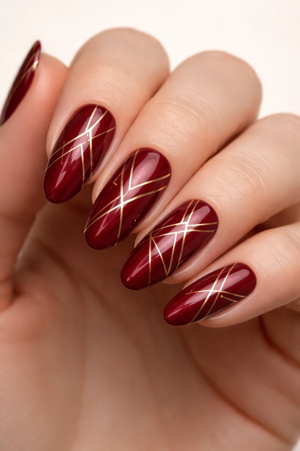 Close-up of long round nails with deep red base and gold geometric lines