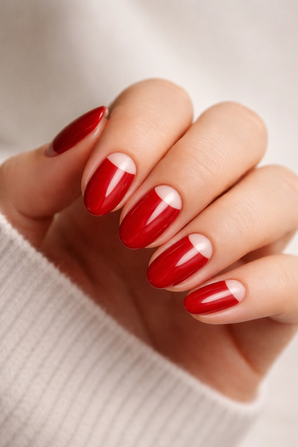 Close-up of short almond nails with cherry red color and negative-space half-moons at the base