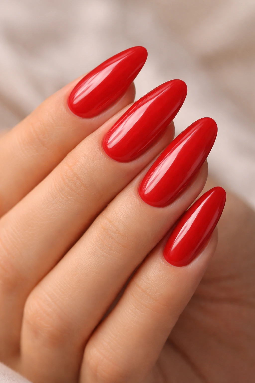 Close-up of bold red long oval acrylic nails on a hand with a neutral background