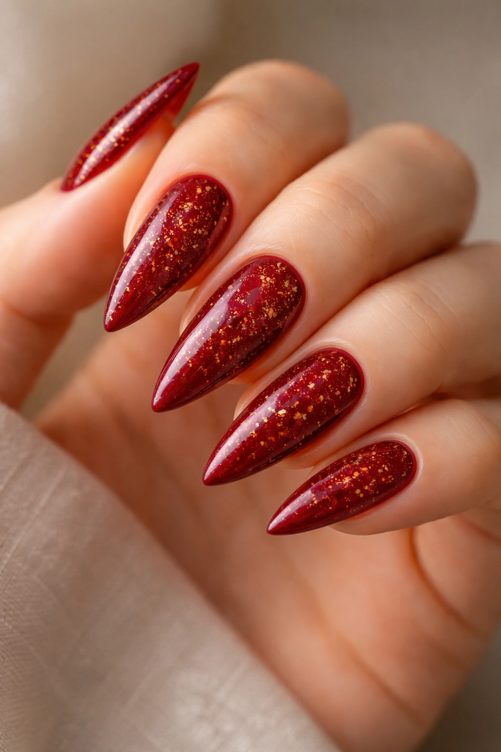 Close-up of medium-length stiletto nails in deep red with gold flecks.
