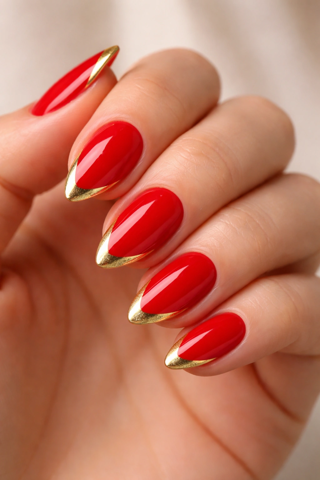 Close-up of short almond nails in red with gold V-tip accents
