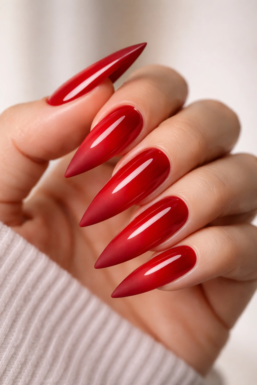 Nail with glossy red base and matte red tip on a stiletto shape