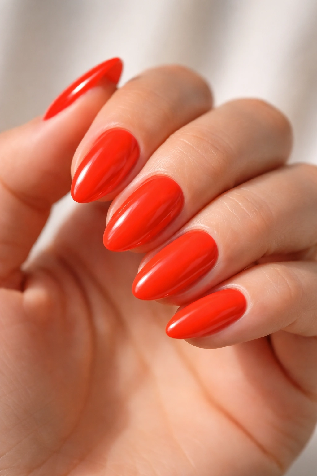 Close-up of short almond nails in bright red-orange with high gloss.