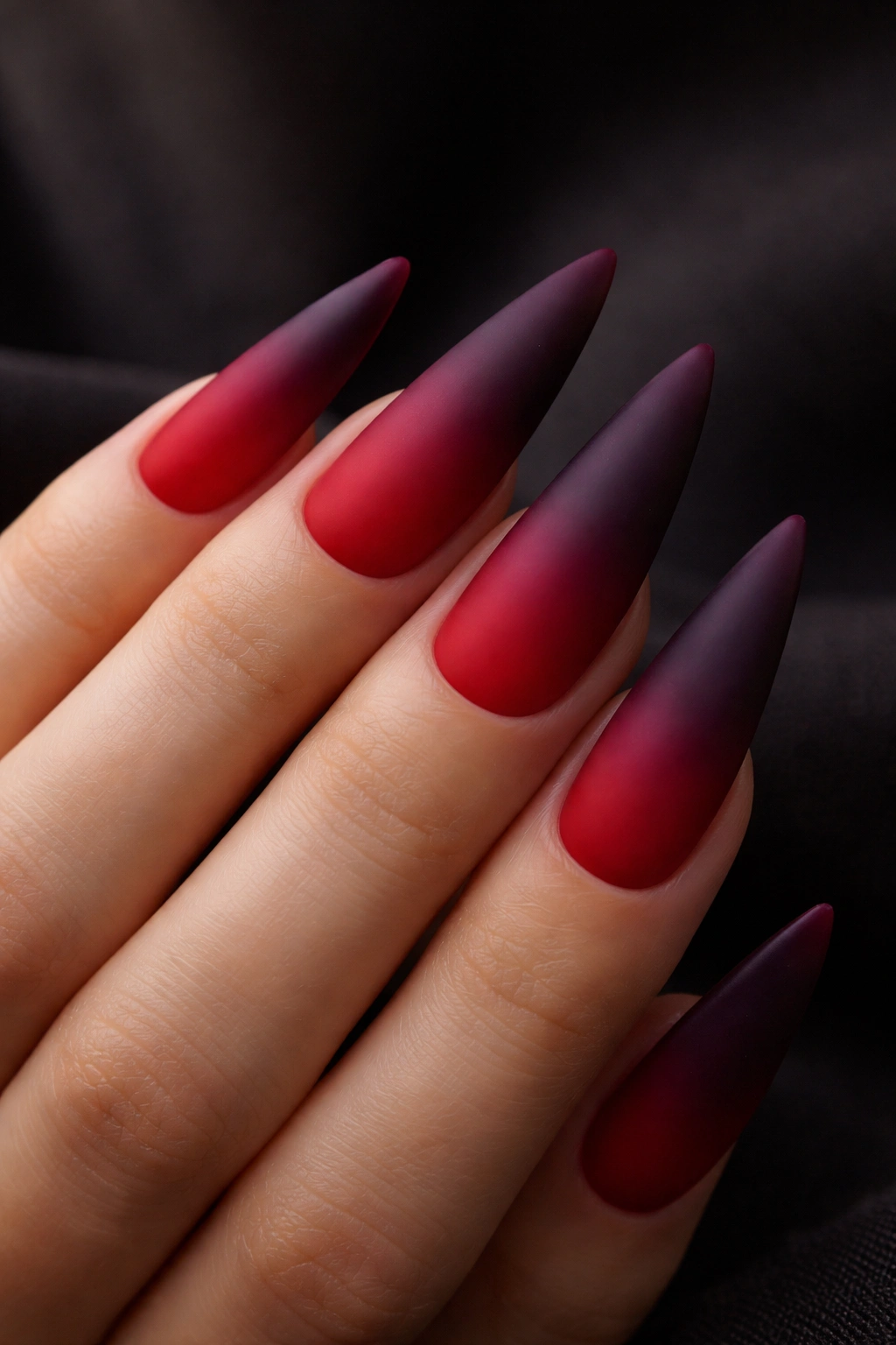 Close-up of matte red to purple ombre stiletto nails on a hand