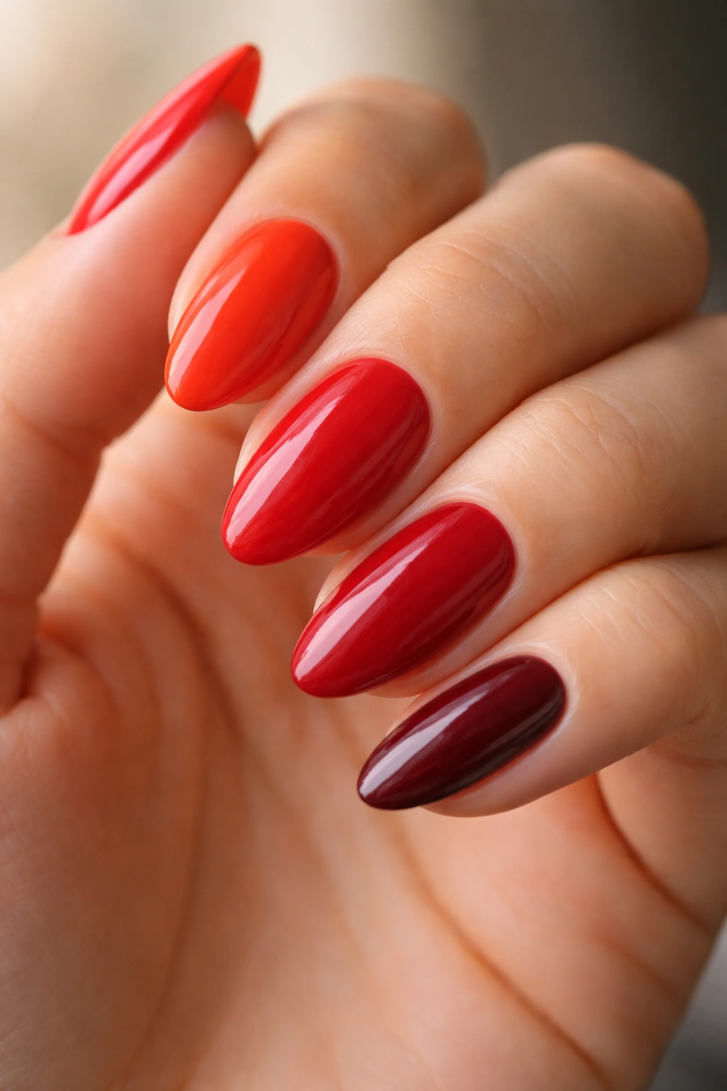Hand with short almond nails in multiple red shades showing undertones