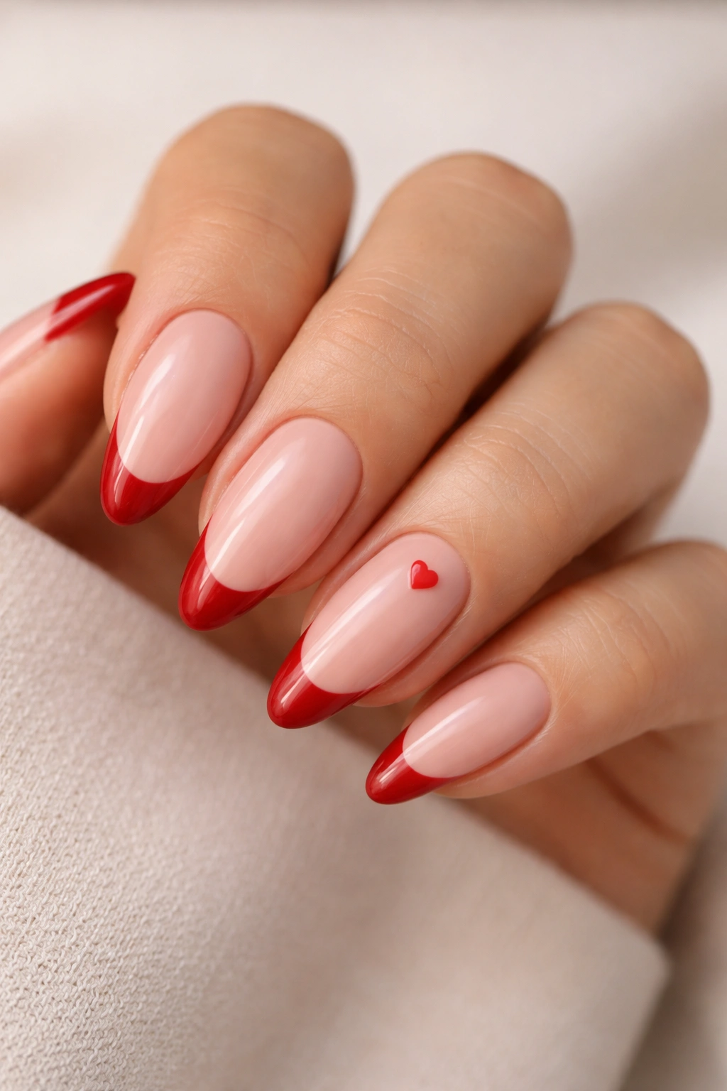 Close-up of almond nails with red tips and tiny heart details