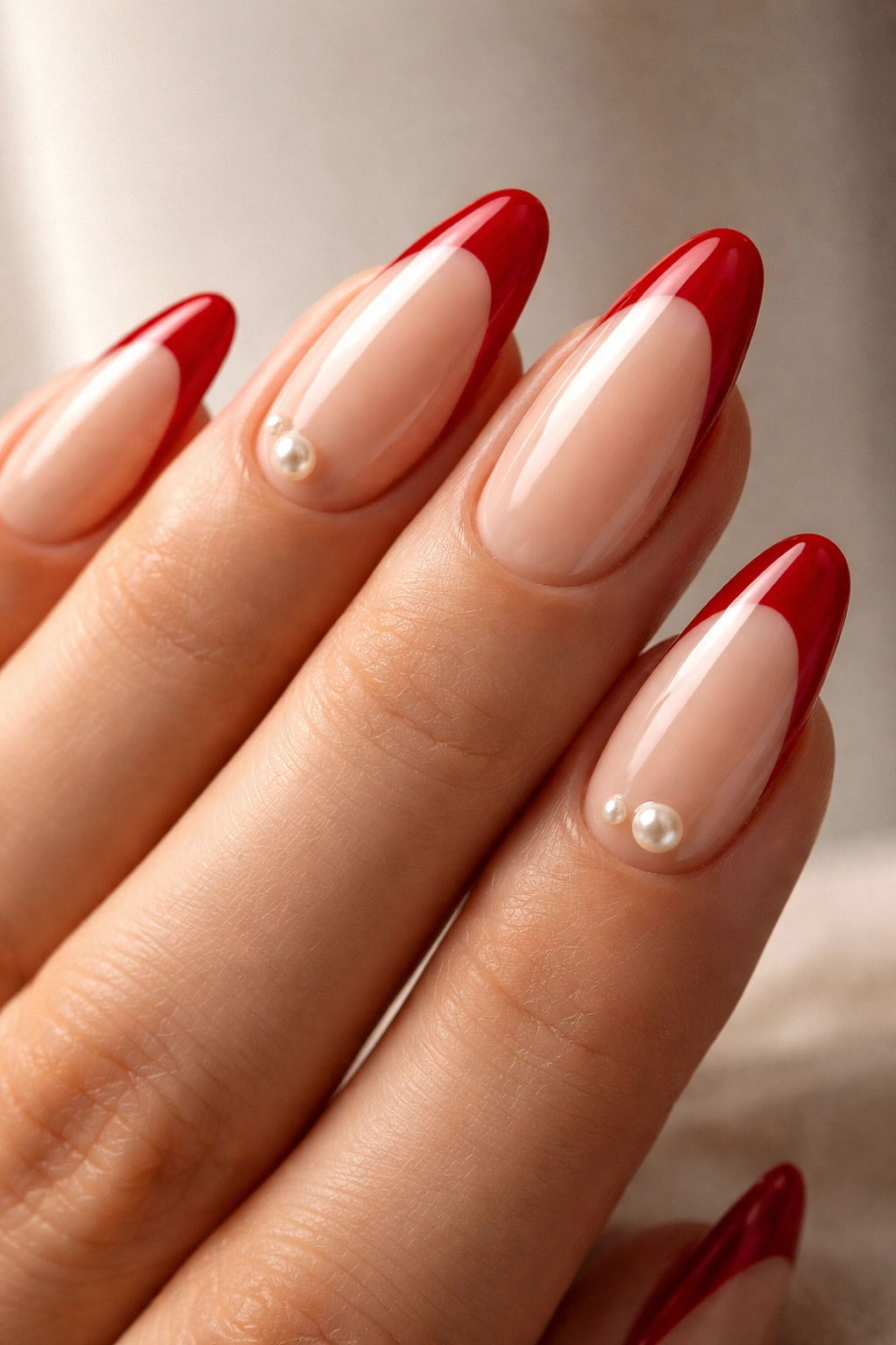 Almond nails with red tips and pearl accents near the base