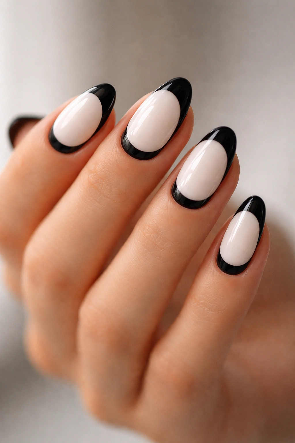 Close-up of reverse French manicure on short almond nails with white nail bed and black tips